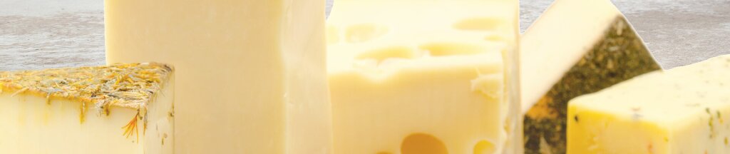 Various pieces of sliced cheese in different shapes and varieties, including cheeses with holes and a herb-coated rind.